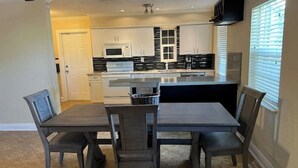 A modern kitchen with white cabinets, a black countertop, and a dining area with a table and chairs. - Margate Zen Paradise Water View (Margate)