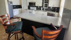 A kitchen with white cabinets, a black countertop, a white stove, and a refrigerator. There are two wooden chairs with green cushions. - Margate Zen Paradise Water View (Margate)
