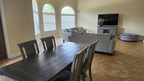 A dining area with a dark wooden table and chairs, a gray sofa, and a television on a stand. - Margate Zen Paradise Water View (Margate)