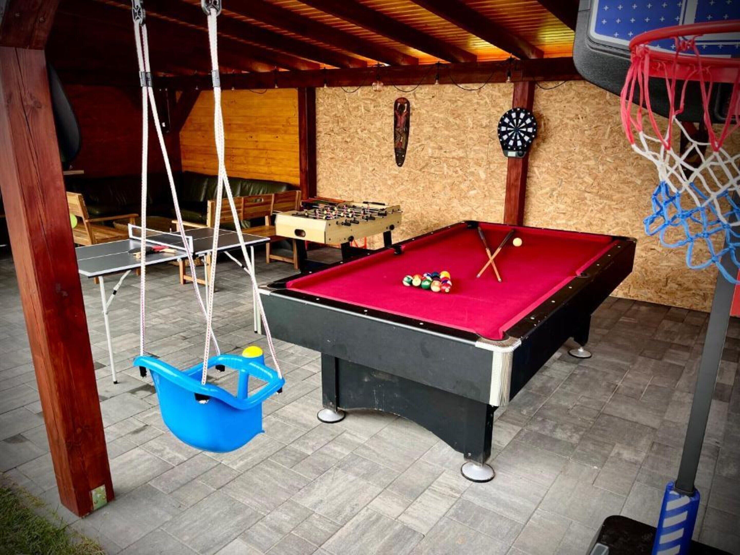 Una mesa de billar con bolas, una mesa de futbolín y un dardo en una sala con techo de madera y suelo de baldosas.