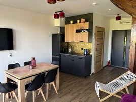 Una cocina compacta con armarios de madera, un refrigerador negro y una pequeña isla con pileta. Hay una mesa de comedor con sillas y una silla colgante.