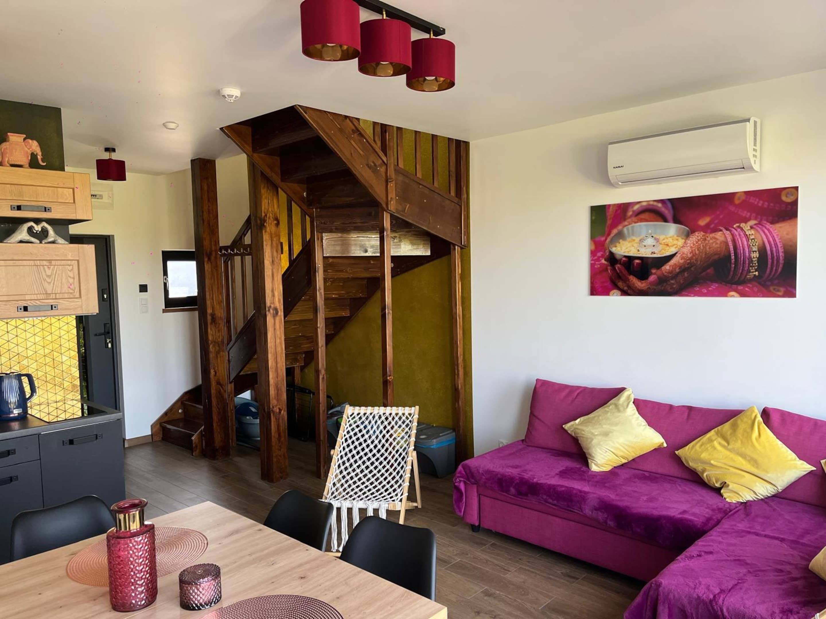 A cozy living area with a purple sofa, a wooden staircase, and a dining table with chairs.