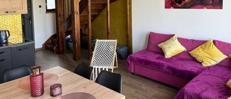 A cozy living area with a purple sofa, a wooden staircase, and a dining table with chairs.