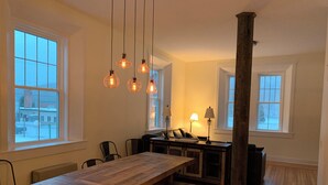 Una cocina amplia con una mesa de madera y bancos, ventanas grandes y lámparas colgantes.