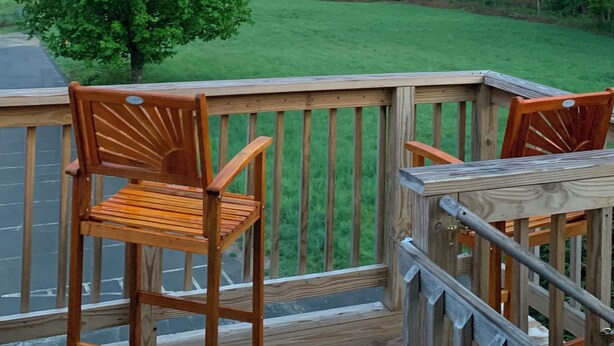 Una terraza de madera con dos sillas y una mesa, con vistas a un paisaje verde con un árbol y colinas.