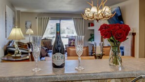 A bar area with a wine bottle, two glasses, and a vase with red roses.