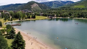 A lake surrounded by mountains, a sandy beach, and buildings in the background.