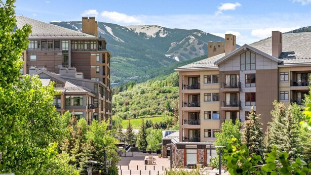 A modern hotel with multiple floors, balconies, and a view of a mountainous landscape.