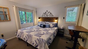 Un dormitorio con cama, escritorio y dos ventanas.