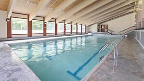 Una piscina interior con agua cristalina, vigas de madera en el techo y suelo de piedra.