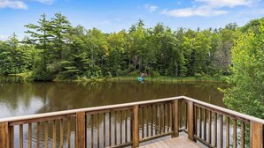Una terraza de madera con vistas a un lago tranquilo, rodeada de un bosque frondoso.