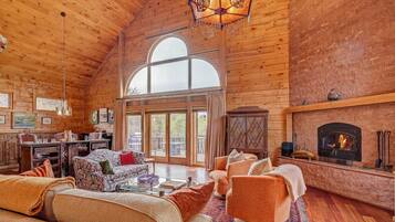 A spacious log cabin interior with a fireplace, large windows, and a cozy seating area.