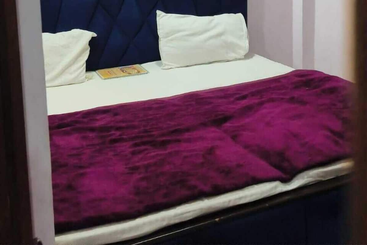 Quarto com cabeceira azul, almofadas brancas e colcha roxa.