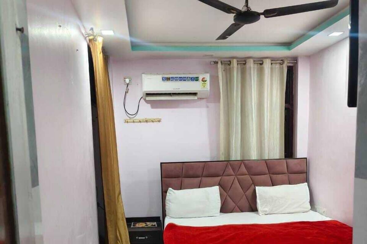 Quarto com cama, ventilador de teto, ar condicionado e janela com cortinas.