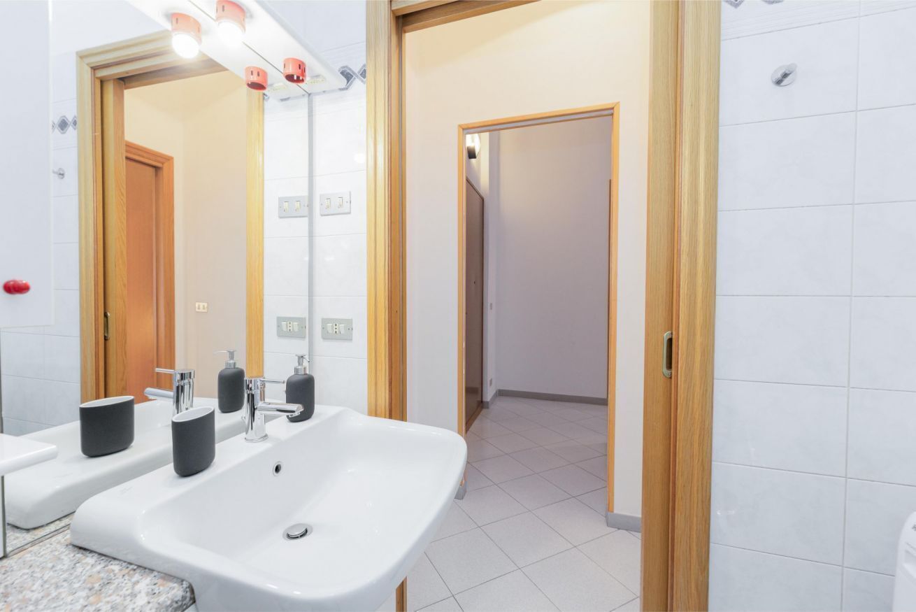 A modern bathroom with a large sink, two mirrors, and a wooden door.