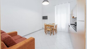 A modern kitchen with white cabinets, a dining table with chairs, and a TV mounted on the wall.