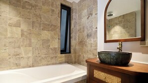 Un baño con bañera, un tocador de madera con un cajón de mimbre y un espejo sobre el tocador.