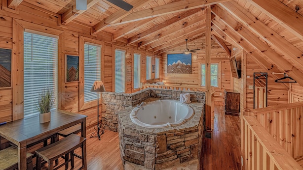 A log cabin interior with a stone bathtub, wooden walls, and a ceiling fan. - Romantic Cabin • Hot Tub • Pond View • Easy Roads • 5 Min to Parkway (Pigeon Forge)
