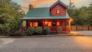 A log cabin with a green metal roof, a front porch, and a chimney. - Romantic Cabin • Hot Tub • Pond View • Easy Roads • 5 Min to Parkway (Pigeon Forge)