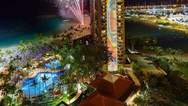 Un hôtel de grande hauteur doté d’une piscine et offrant une vue sur la plage, illuminé par des feux d’artifice.