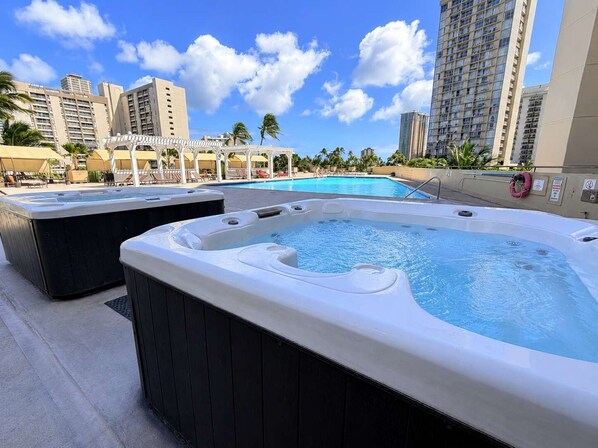 A rooftop pool area with hot tubs and a view of high-rise buildings.