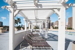 Zona de piscina en la azotea con tumbonas y una pérgola.