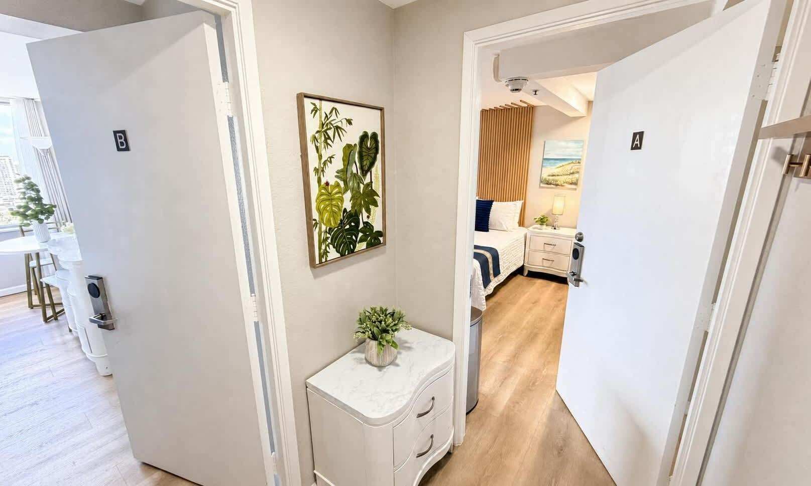 Una habitación de hotel con una cama, una mesita de noche y un pequeño armario blanco.