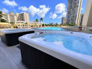 A rooftop pool area with hot tubs and a view of high-rise buildings.