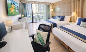 A hotel room with a desk, two beds, a TV, and a balcony with a view of buildings.