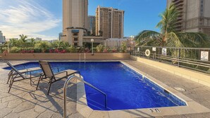 A rooftop pool with lounge chairs, surrounded by palm trees and a cityscape with tall buildings. - Waikiki Ocean View Studio, 3 Beds, Block to Beach (Honolulu)