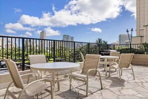 An outdoor patio with round tables and chairs, a black metal fence, and a view of tall buildings in the background.