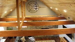 A loft-style room with exposed wooden beams, a stone fireplace, and a large wall clock.
