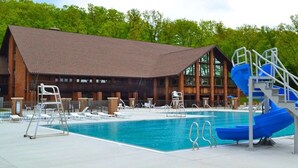 A swimming pool area with a wooden building, lounge chairs, and a blue slide.
