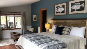 A bedroom with a large bed, a chair, a nightstand, and a window with curtains.