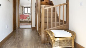 Een houten trap met een rieten stoel onderaan. Een gang leidt naar een kamer met een bed en een raam.