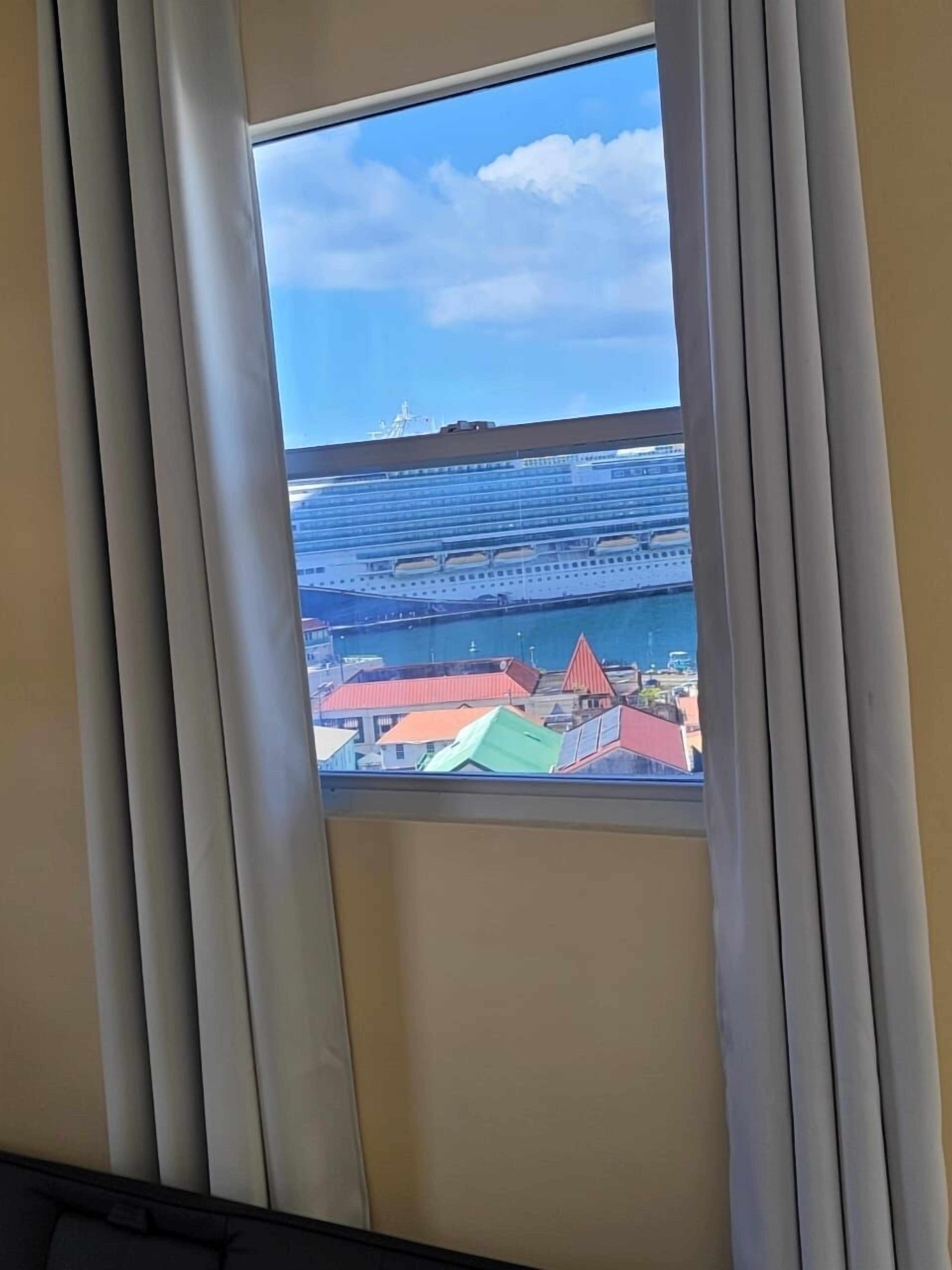 A window view of a cruise ship docked at a port with colorful buildings in the foreground.