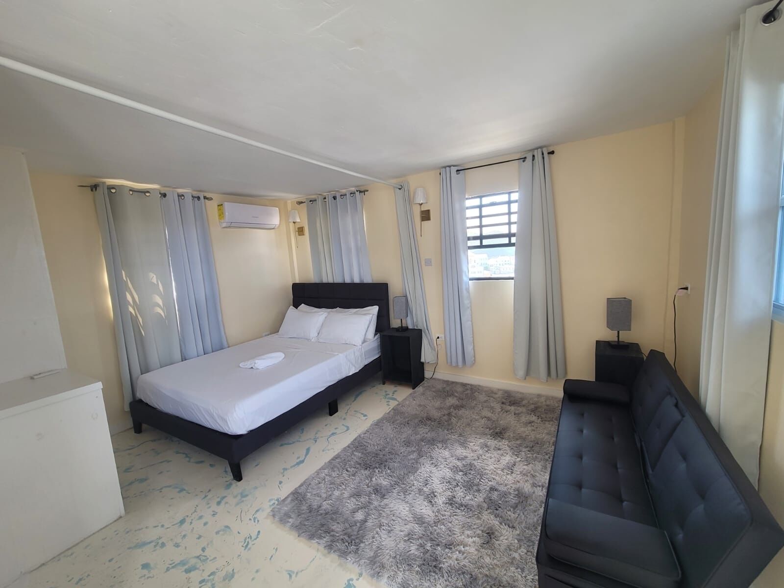 A bedroom with a bed, a sofa, a small table with a lamp, and a window with curtains.