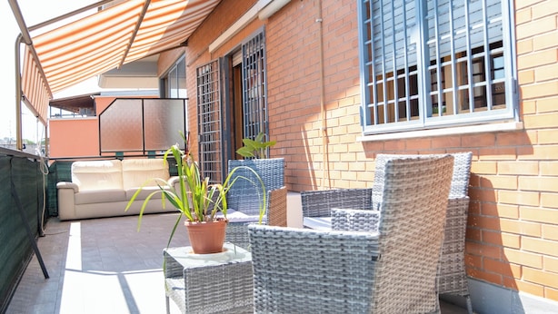 A patio with wicker furniture, a potted plant, and a brick wall. - LtPanella Jacqueline (Roma)