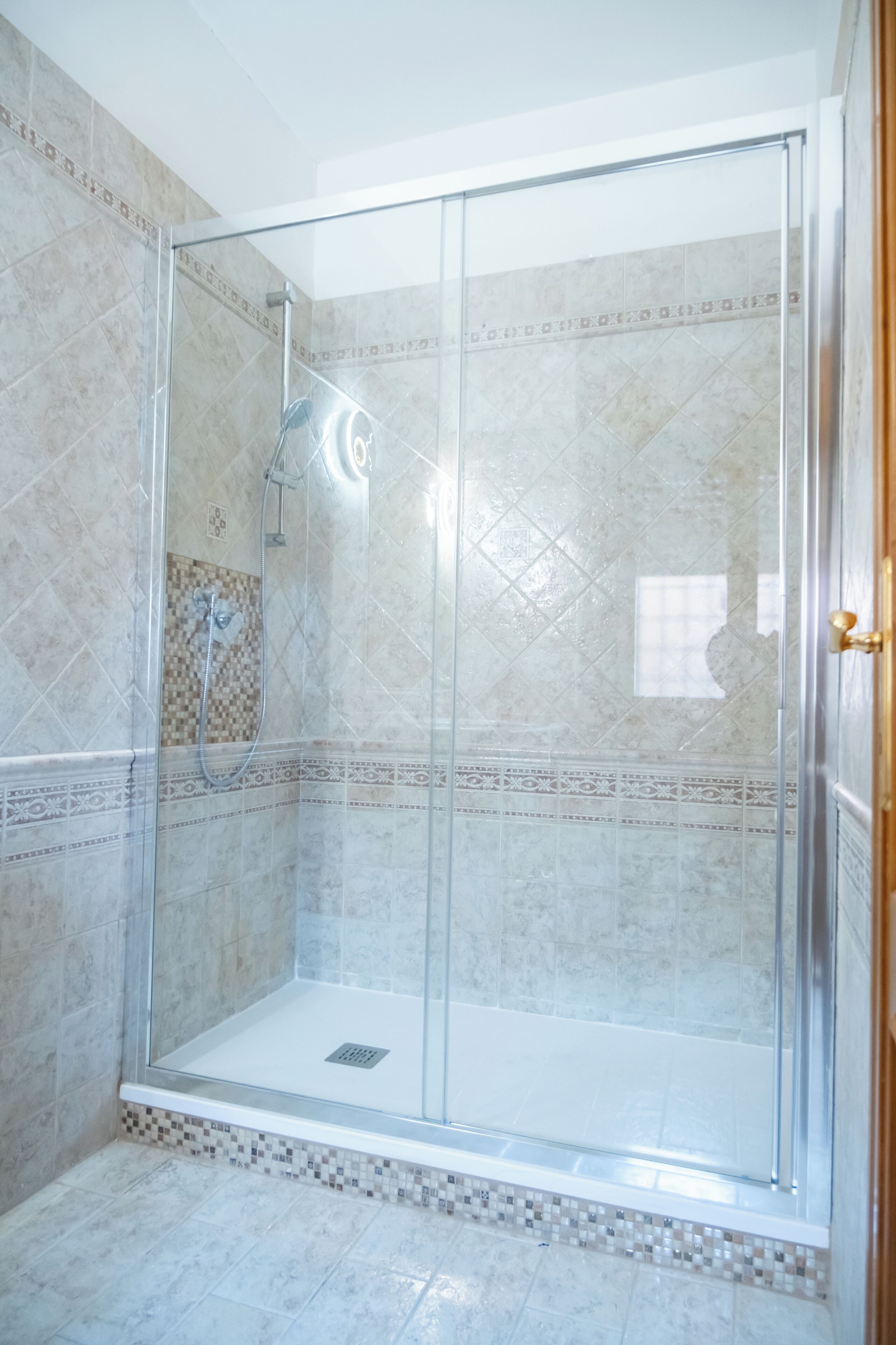 A glass-enclosed shower area with tiled walls and a patterned border.