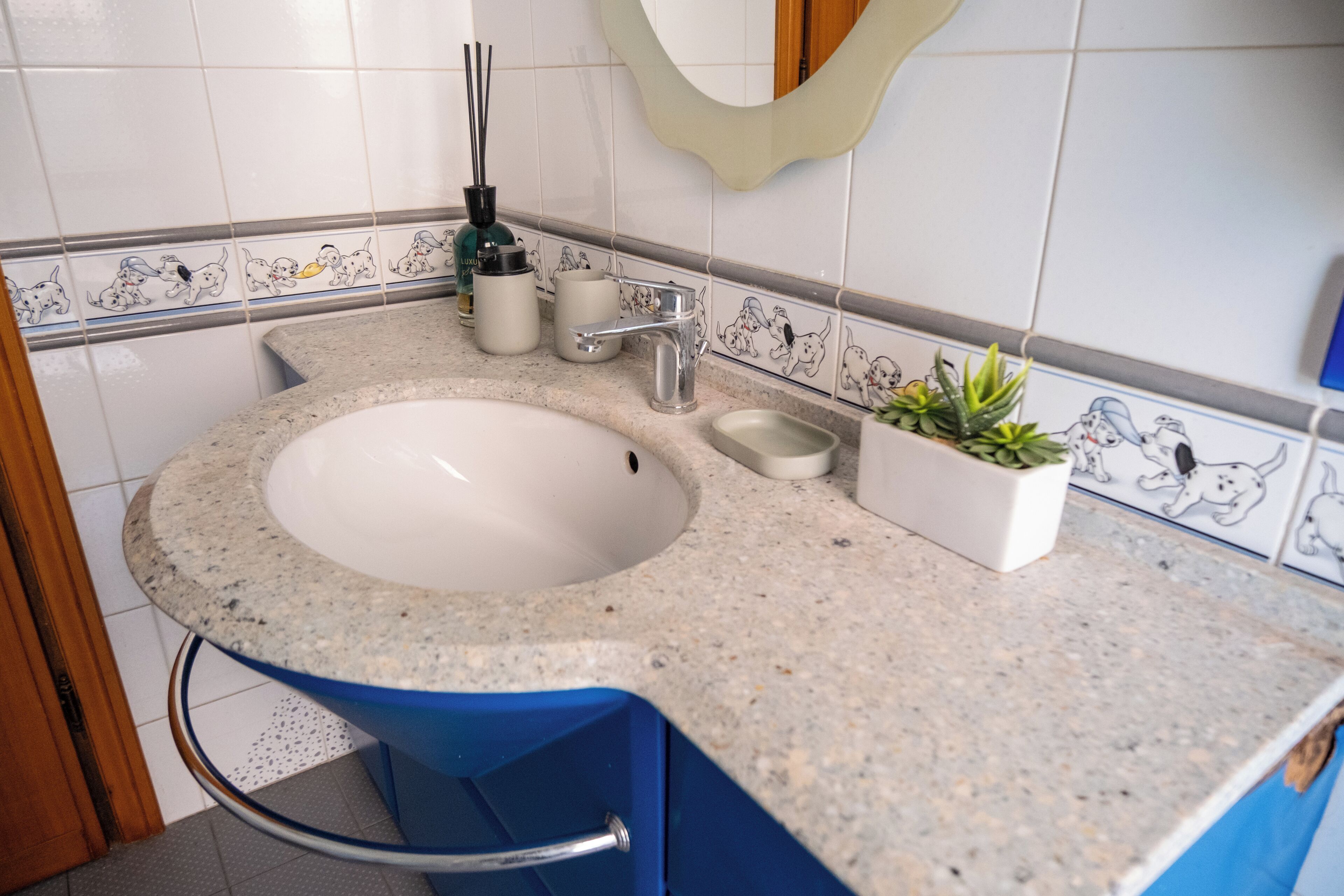 Un baño con un lavamanos blanco, una silla azul y un borde decorativo de azulejos.