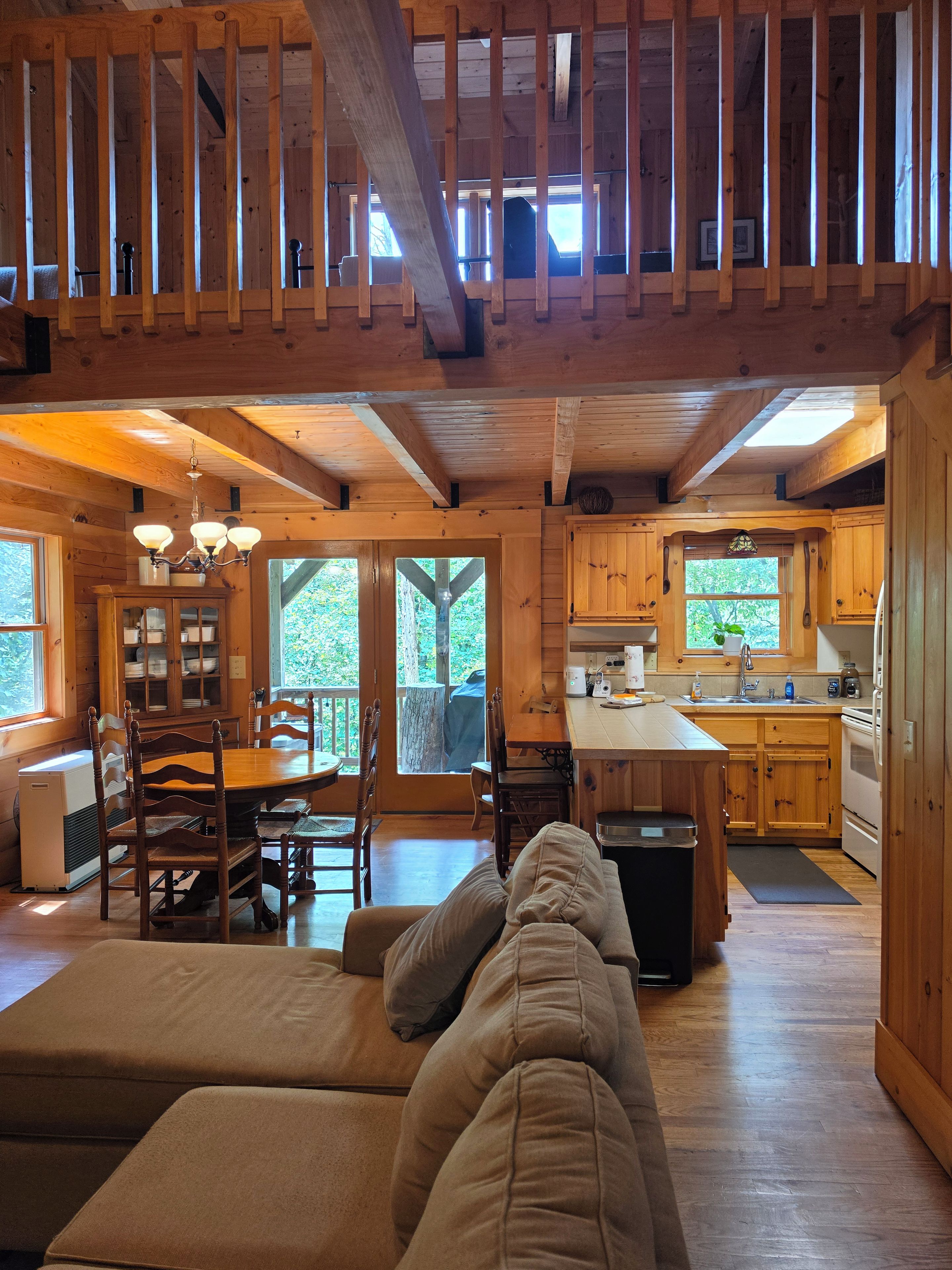 Un interior de cabaña espacioso con comedor, cocina y habitación en altillo.