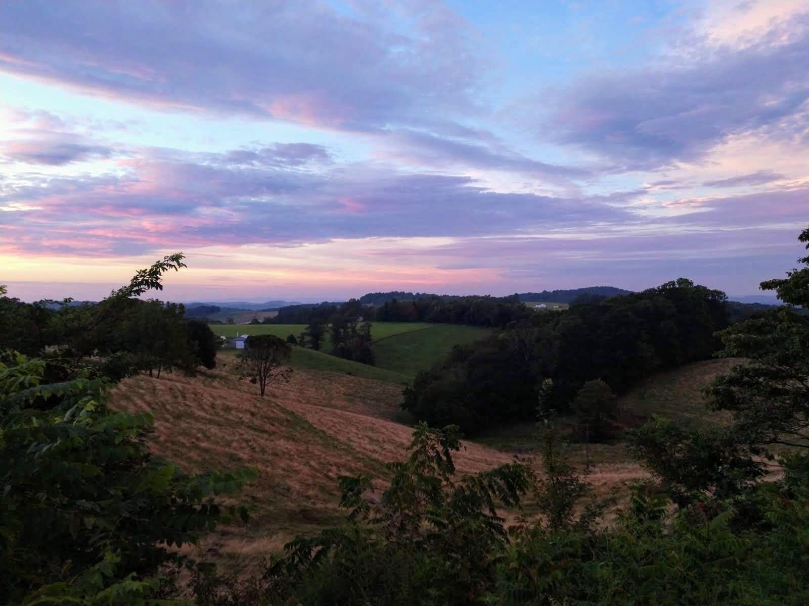 A rural landscape with rolling hills, trees, and a clear sky.