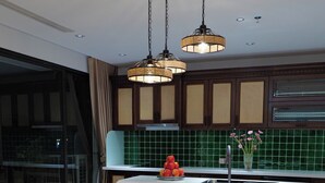 A modern kitchen with a dining area, featuring a long wooden table set for six, hanging pendant lights, and a green tiled backsplash. - Ho Tay Residences (Hanoi)