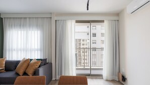A modern living room with a grey sofa, two brown chairs, a white coffee table, and a large sliding glass door leading to a balcony. - Bothanic Campo Belo by Wecare Hosting (São Paulo)