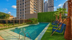 A swimming pool with a metal ladder, surrounded by a green hedge and palm trees. - Bothanic Campo Belo by Wecare Hosting (São Paulo)