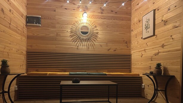 A wooden interior with a bench, a table, and a wall-mounted light fixture. - THE NATURAL PATIO (Saint-Étienne)