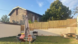 A backyard with a stone house, a wooden fence, and outdoor furniture including a table and chairs. - THE NATURAL PATIO (Saint-Étienne)