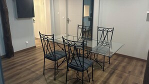 A dining area with a glass table and four chairs, wooden flooring, and a door with a mirror. - THE NATURAL PATIO (Saint-Étienne)