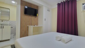 Habitación de hotel con cama, televisor montado en la pared, armario y ventana con cortinas.