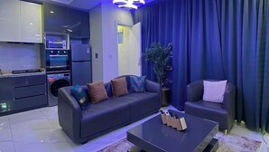 Een moderne woonkamer met een donkere bank, een salontafel en een groot raam met blauwe gordijnen.